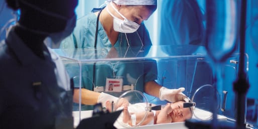 Medical professionals with preterm baby in incubator