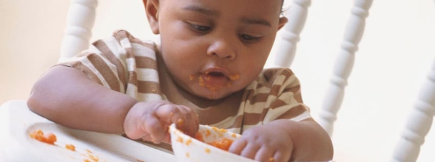 Baby eating with fingers from bowl