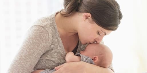 woman comforting and kissing a newborn on the forehead