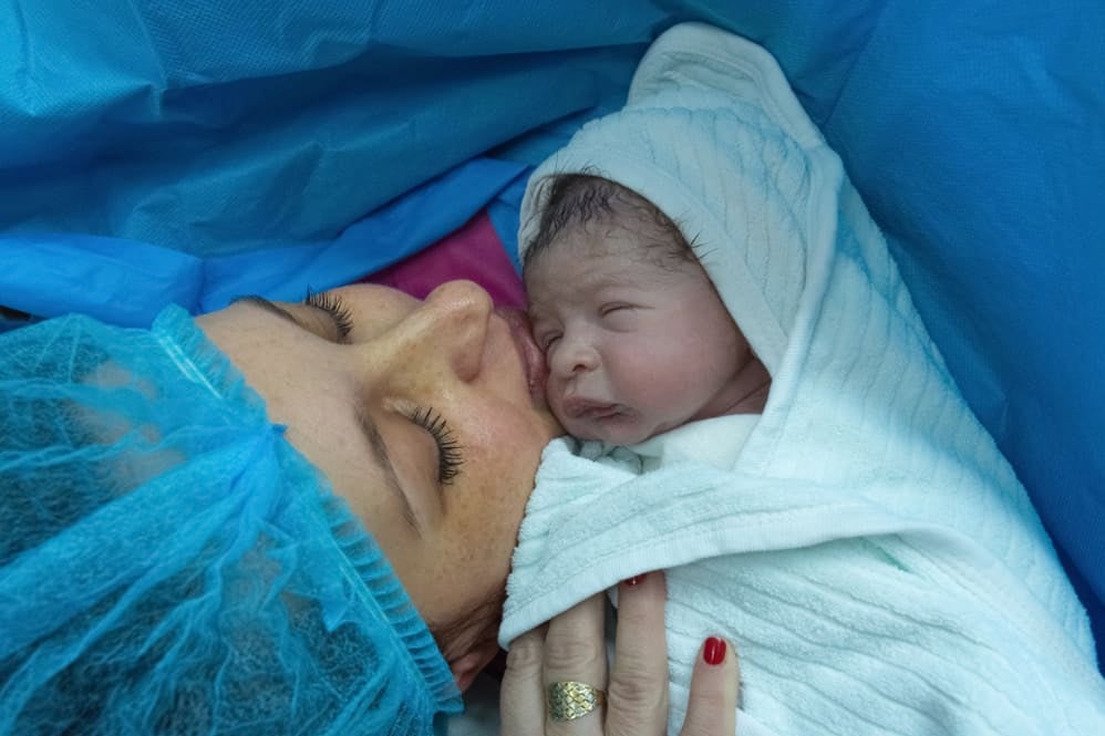 Mother in blue scrubs holding her baby wrapped in a towel post caesarean