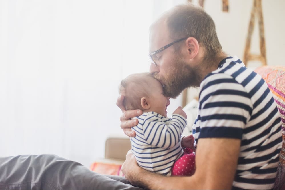 Father gently kissing his crying baby's forehead
