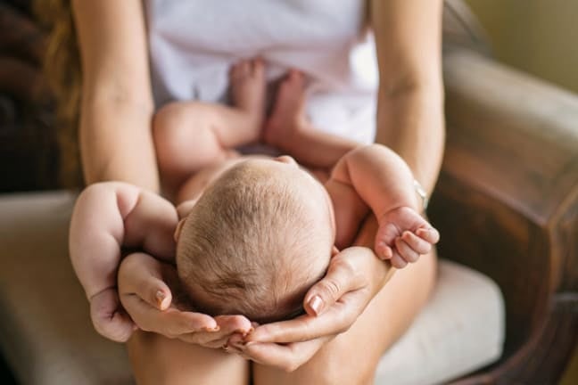 Mother cradling the head of a baby lying on her lap