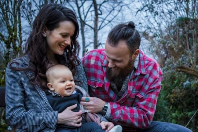 Laughing parents in a park holding a baby