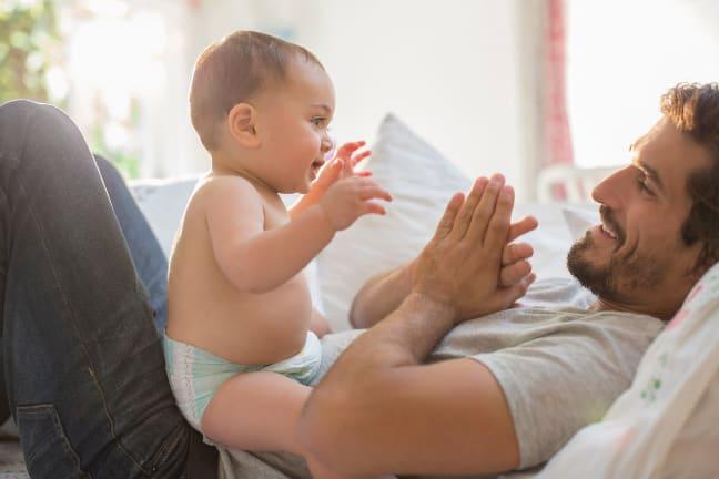 Baby sitting on parents lap smiling and clapping hands