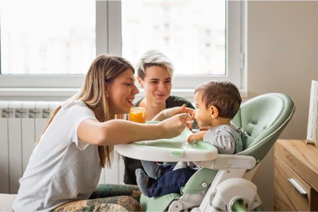 Two women feeding a toddler who is in a high chair