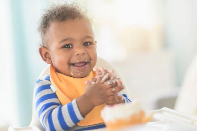 Child sitting in high chair with a bib round his neck and food smeared over his mouth and hands