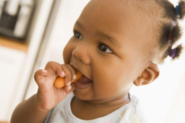 Toddler eating a carrot wearing a light coloured top